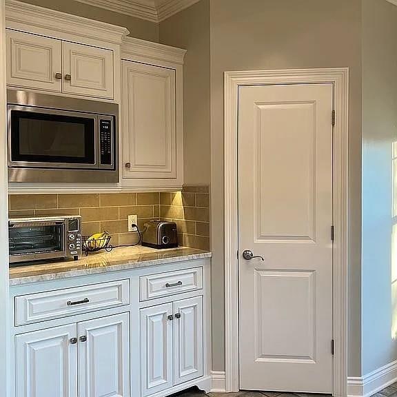 kitchen featuring stainless steel microwave, decorative backsplash, white cabinetry, and a toaster