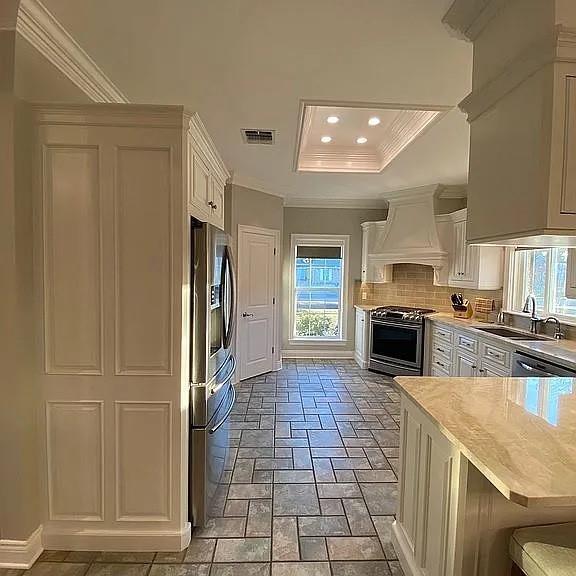 kitchen featuring white cabinets, ornamental molding, a sink, appliances with stainless steel finishes, and custom exhaust hood