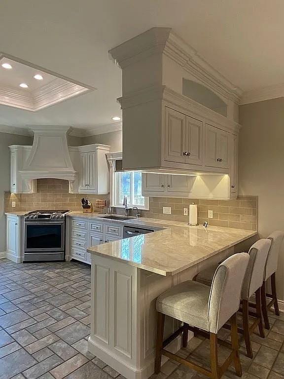 kitchen with stainless steel range with gas cooktop, crown molding, decorative backsplash, a peninsula, and custom exhaust hood