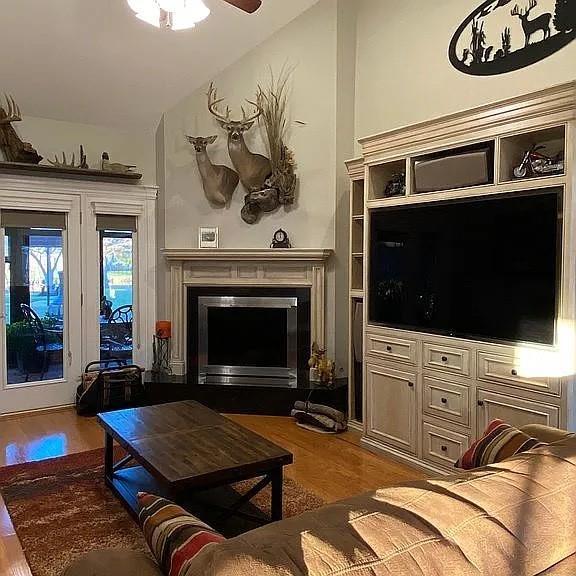 living area featuring a glass covered fireplace, vaulted ceiling, wood finished floors, and a ceiling fan