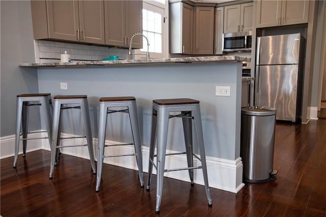 1529 Saint Philip St, New Orleans, LA 70116 - kitchen featuring stainless steel appliances, gray cabinetry, tasteful backsplash, a breakfast bar, and dark wood-type flooring