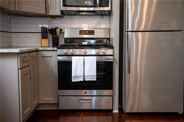 1529 Saint Philip St, New Orleans, LA 70116 - kitchen featuring appliances with stainless steel finishes, gray cabinets, dark wood finished floors, backsplash, and light stone counters