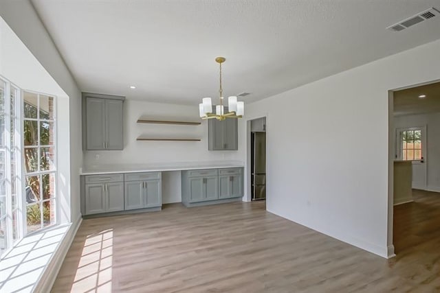unfurnished dining area featuring visible vents, baseboards, a notable chandelier, and light wood-type flooring