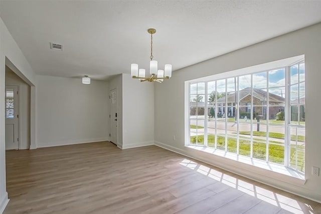 unfurnished dining area with wood finished floors, baseboards, a chandelier, and visible vents