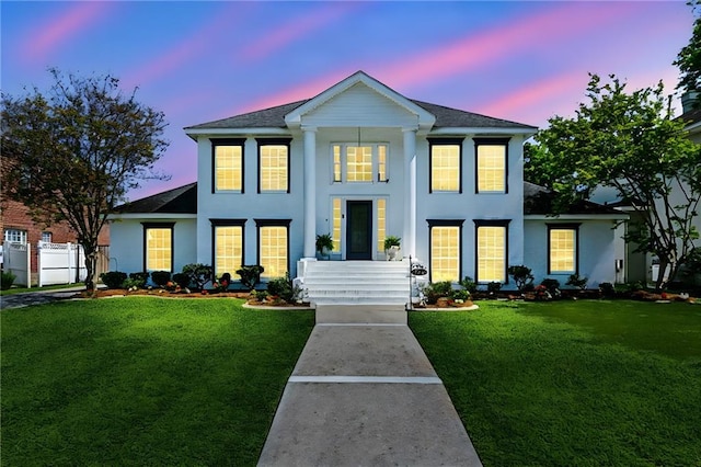 neoclassical / greek revival house with a lawn, stucco siding, and roof with shingles