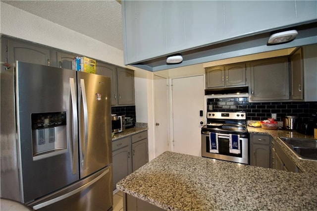 3209 Jennifer Ct, Marrero, LA 70072 - kitchen featuring stainless steel appliances, under cabinet range hood, tasteful backsplash, a peninsula, and light stone countertops