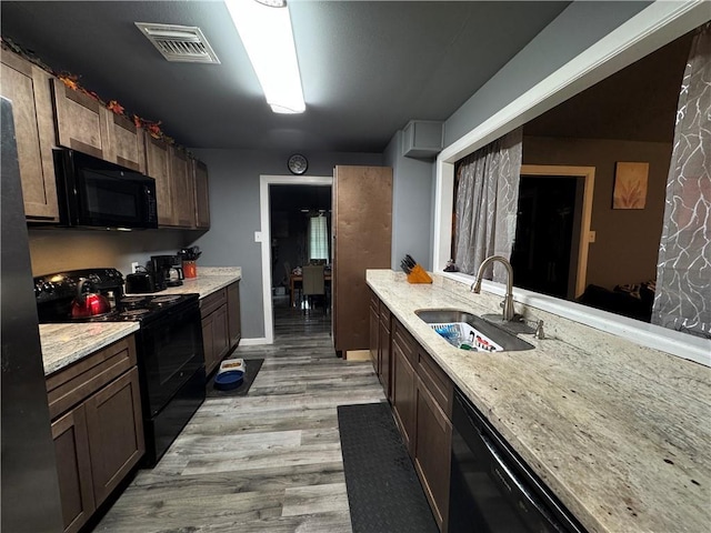 kitchen with light stone countertops, light wood-style floors, black appliances, a sink, and visible vents