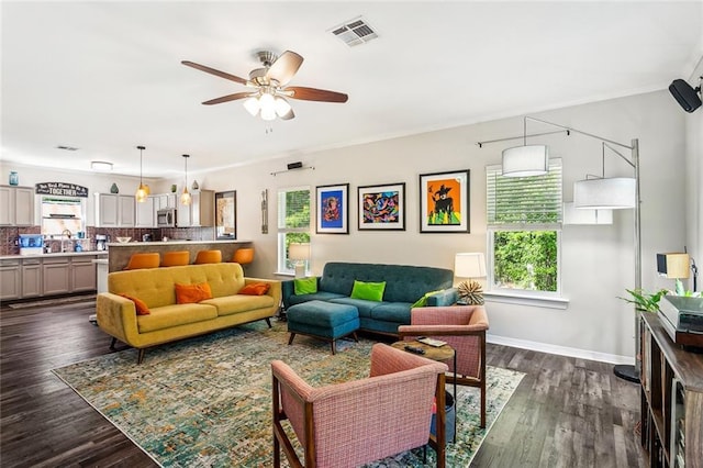 living room featuring a ceiling fan, dark wood finished floors, baseboards, ornamental molding, and visible vents