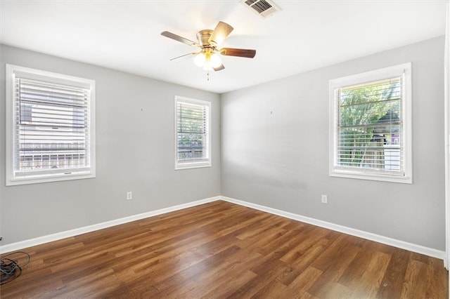 unfurnished room featuring a wealth of natural light, wood finished floors, visible vents, and baseboards