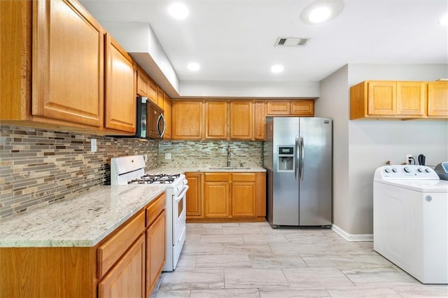 kitchen featuring visible vents, white range with gas stovetop, a sink, washer / dryer, and stainless steel refrigerator with ice dispenser