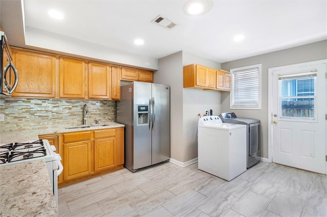 kitchen featuring stainless steel fridge, a sink, tasteful backsplash, visible vents, and independent washer and dryer