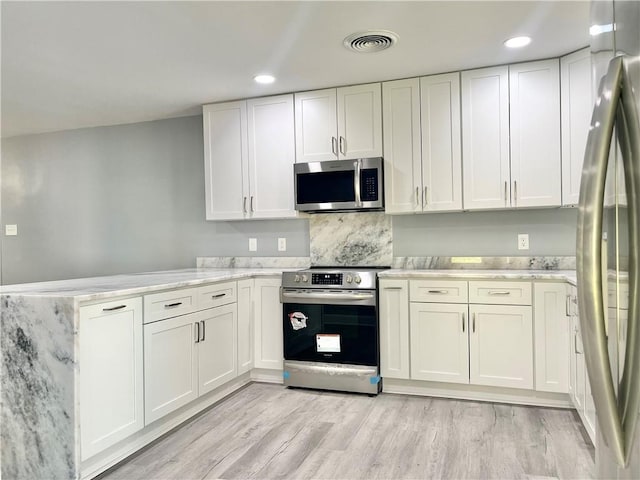 kitchen with appliances with stainless steel finishes, white cabinetry, and a peninsula