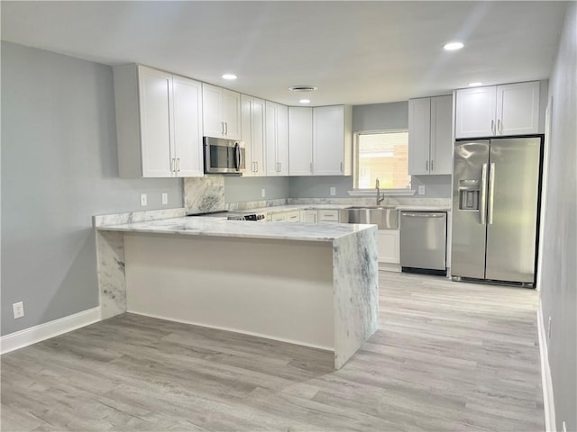 kitchen with stainless steel appliances, light wood-style floors, white cabinets, a sink, and a peninsula