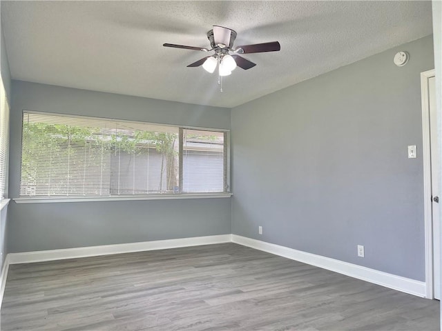 empty room featuring a textured ceiling, ceiling fan, a wealth of natural light, and wood finished floors