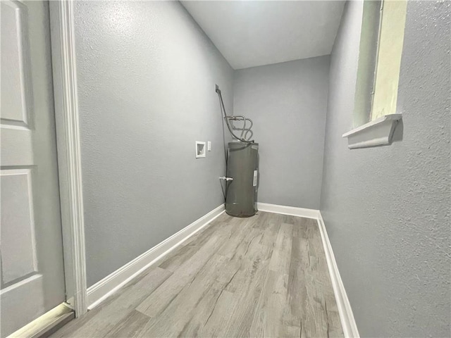 washroom with baseboards, hookup for a washing machine, water heater, wood finished floors, and laundry area