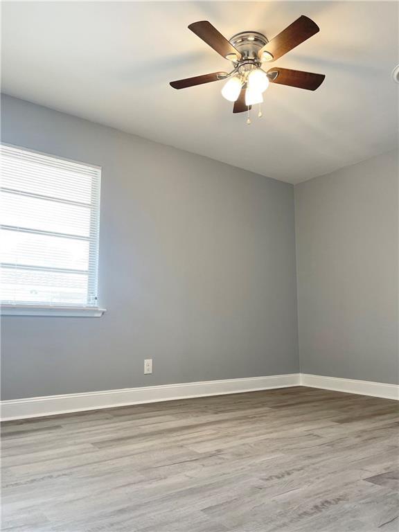 empty room with ceiling fan, wood finished floors, and baseboards