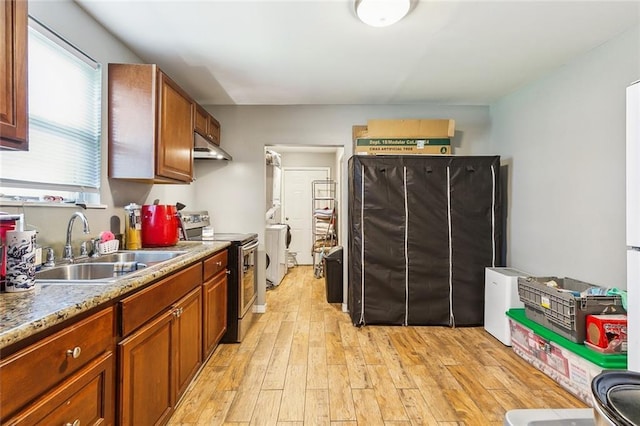 kitchen featuring under cabinet range hood, a sink, light wood-type flooring, stainless steel electric stove, and washer / clothes dryer