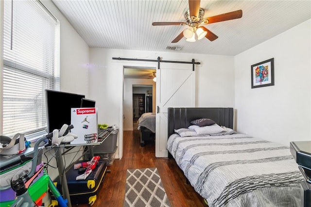 bedroom featuring a barn door, wood finished floors, visible vents, and a ceiling fan