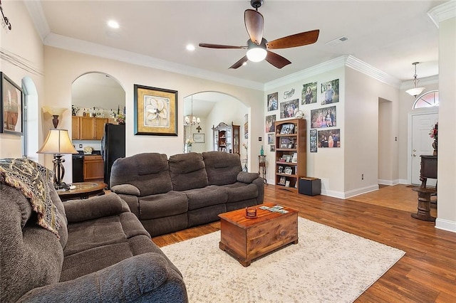 living area with arched walkways, crown molding, wood finished floors, and a ceiling fan