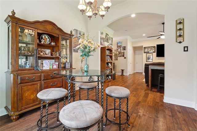 bar featuring arched walkways, ornamental molding, dark wood-style floors, and ceiling fan with notable chandelier