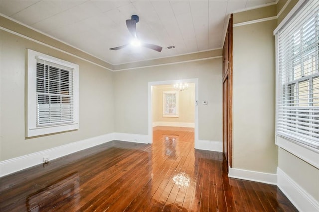 spare room with visible vents, ornamental molding, wood-type flooring, baseboards, and ceiling fan with notable chandelier