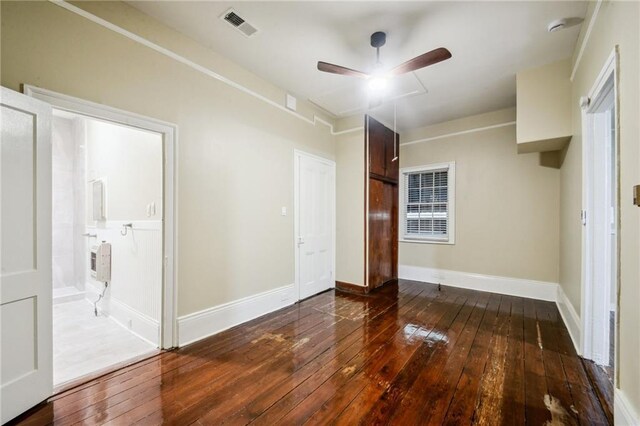 unfurnished bedroom featuring a ceiling fan, connected bathroom, baseboards, dark wood-type flooring, and visible vents