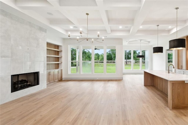 unfurnished living room with a tile fireplace, light wood finished floors, coffered ceiling, beamed ceiling, and a notable chandelier
