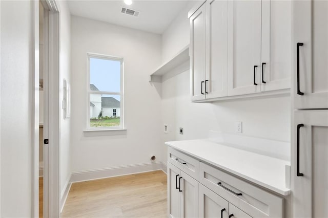 laundry room with hookup for an electric dryer, light wood-type flooring, cabinet space, baseboards, and visible vents