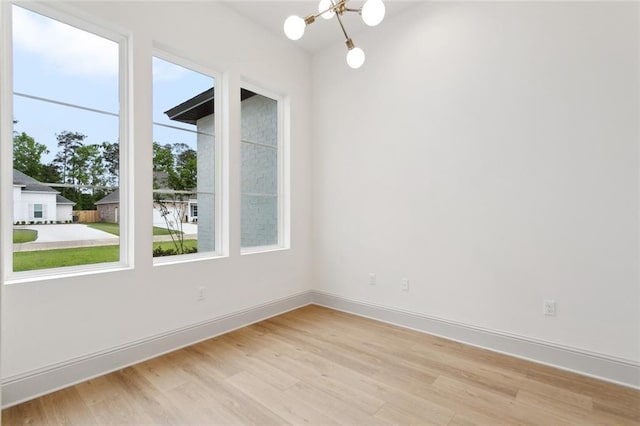 spare room with baseboards, light wood-style floors, and a notable chandelier
