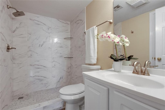 bathroom with vanity, toilet, visible vents, and a tile shower