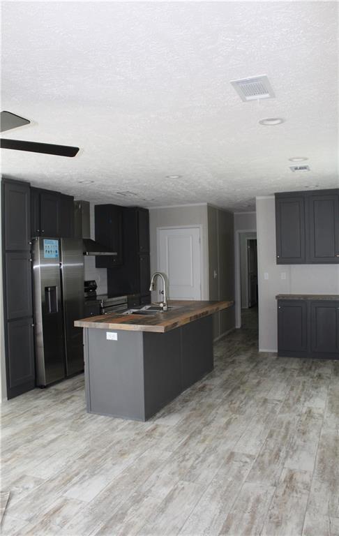 kitchen with a textured ceiling, a sink, visible vents, stainless steel refrigerator with ice dispenser, and wooden counters