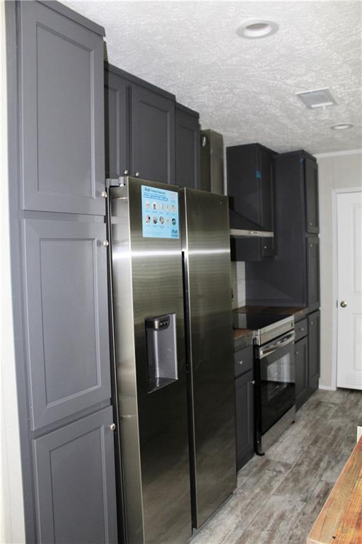 kitchen featuring a textured ceiling, oven, stainless steel fridge with ice dispenser, light wood finished floors, and electric range