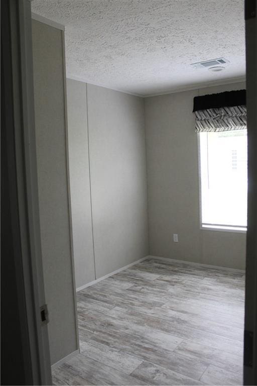 spare room featuring baseboards, wood finished floors, visible vents, and a textured ceiling