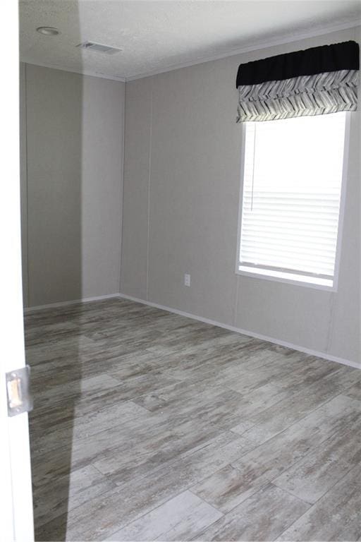 unfurnished room featuring baseboards, wood finished floors, visible vents, and ornamental molding