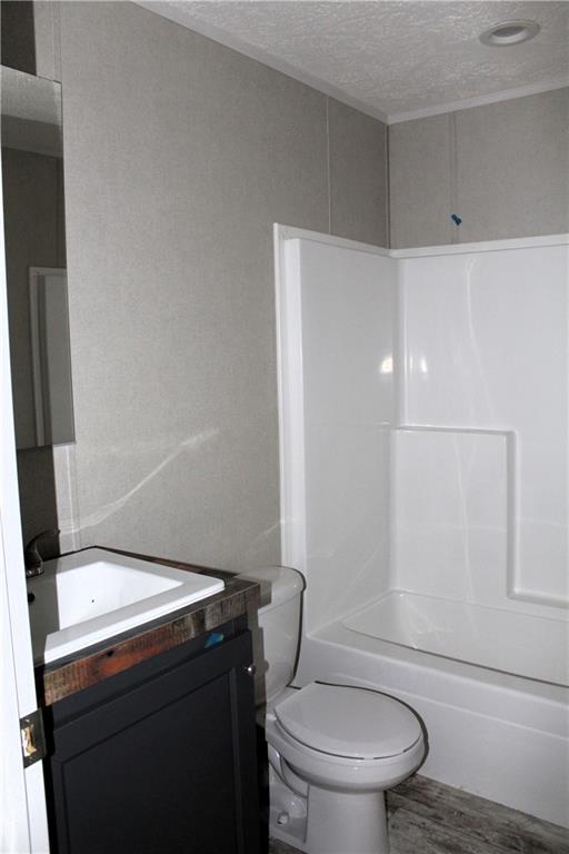 bathroom featuring a textured ceiling, toilet, wood finished floors, washtub / shower combination, and vanity