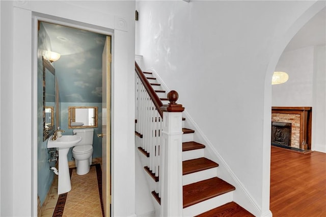 1704 Milan St, New Orleans, LA 70115 - staircase featuring baseboards, arched walkways, wood finished floors, and a fireplace