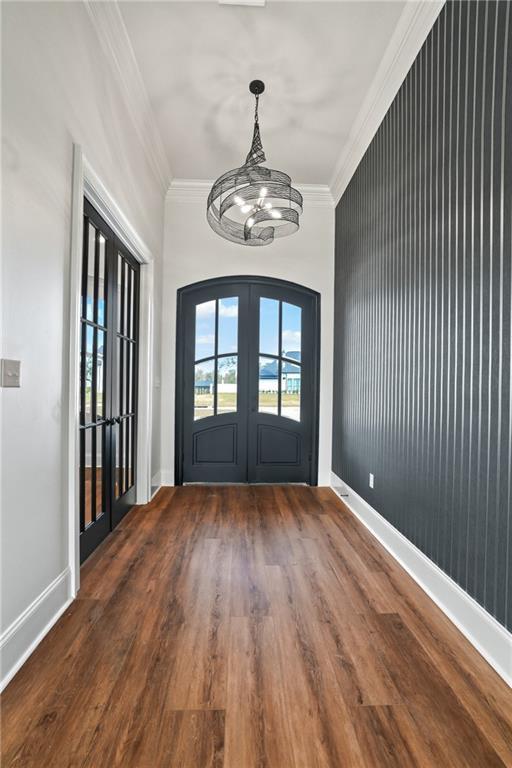 foyer entrance featuring an inviting chandelier, wood finished floors, french doors, and crown molding