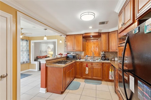 kitchen featuring a sink, brown cabinetry, light tile patterned floors, a peninsula, and appliances with stainless steel finishes