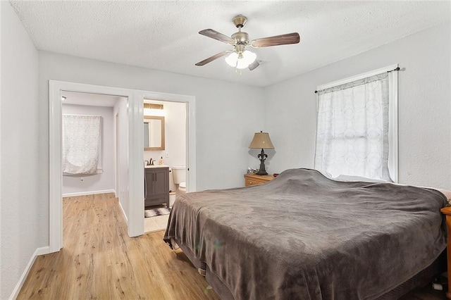 bedroom with ceiling fan, baseboards, ensuite bathroom, and light wood finished floors
