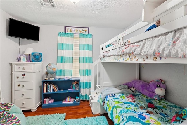 bedroom with a textured ceiling, wood finished floors, and visible vents