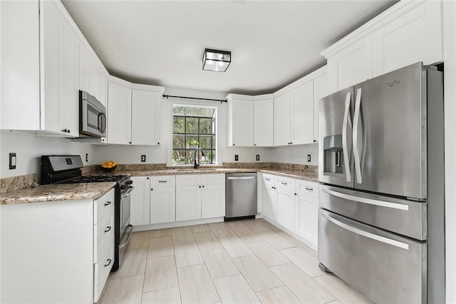 kitchen with white cabinets, light stone counters, stainless steel appliances, and a sink