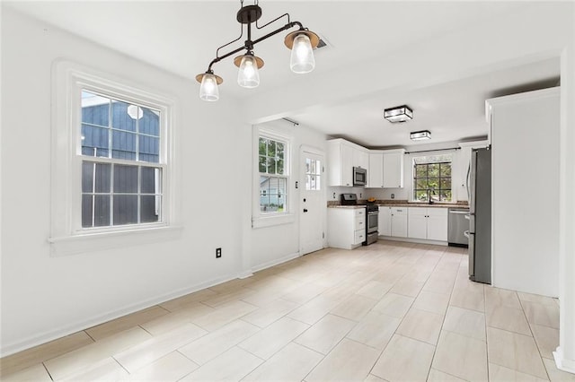 kitchen with a sink, baseboards, pendant lighting, appliances with stainless steel finishes, and white cabinetry