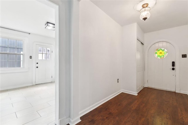 foyer entrance featuring wood finished floors, baseboards, and arched walkways