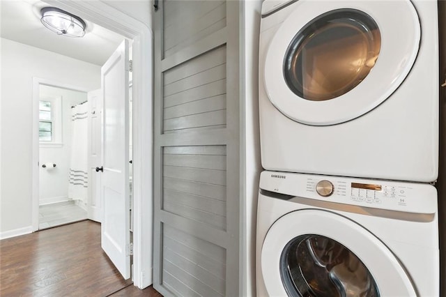 laundry area with stacked washer / drying machine, laundry area, baseboards, and dark wood-type flooring