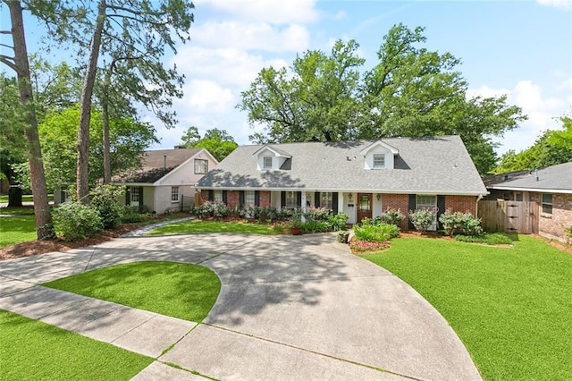 new england style home featuring brick siding, fence, a front yard, and curved driveway