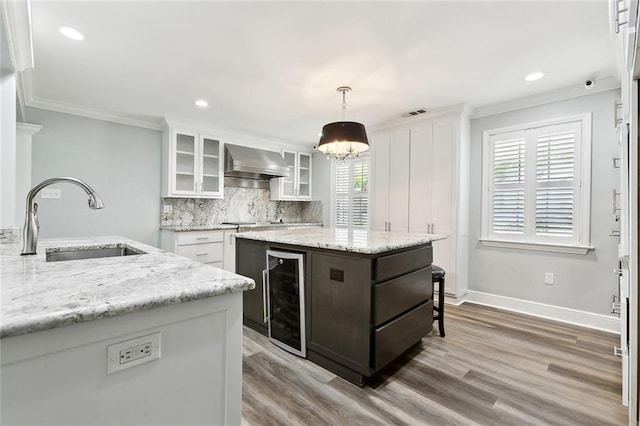 kitchen with wall chimney exhaust hood, white cabinetry, a sink, and wine cooler