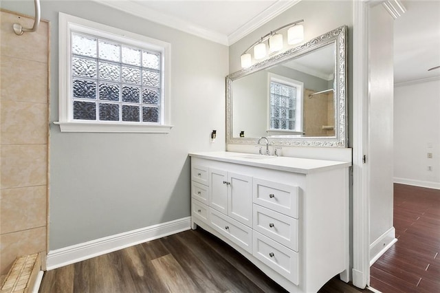 bathroom with a tile shower, wood finished floors, vanity, crown molding, and baseboards