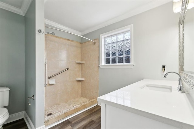 bathroom featuring a tile shower, wood finished floors, toilet, vanity, and crown molding