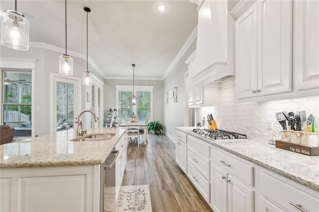 kitchen featuring light wood-style flooring, white cabinets, custom range hood, a sink, and backsplash