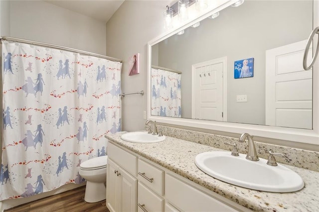 bathroom featuring double vanity, wood finished floors, toilet, and a sink